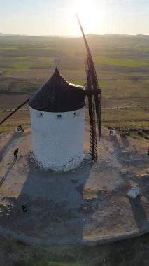 İspanya, Castilla-La Mancha Consuegra 'da günbatımında geleneksel bir rüzgar değirmeni etrafında dönen 4K dikey hava aracı görüntüsü. Kırsal alan üzerinde sıcak altın saat ışığı, seyahat, turizm ve sosyal medya içeriği için ideal.