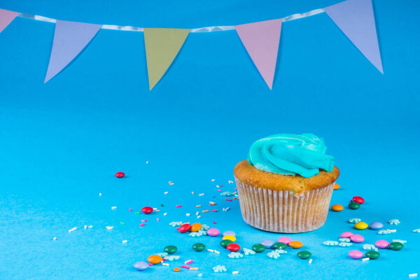 Cupcake with whipped cream in a blue background, decorated with sugar snowflakes, sprinkles, colorful chocolate candies, holiday concept, greeting card