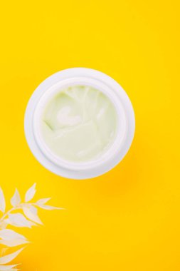Beyaz kavanozda krema ve modaya uygun sarı arka planda yapraklı, kopyalama alanı olan beyaz bir dal. Cilt bakımı kavramı