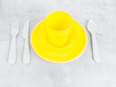 Sarı çatal bıçak takımlarını, tabakları, bardakları, çatalı, kaşığı ve bıçağı son moda gri arka planda aydınlatan piknik malzemeleri. Çevre dostu, geri dönüşüm konsepti için plastik çöp.