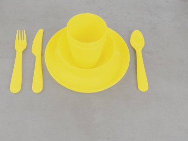 Sarı çatal bıçak takımlarını, tabakları, bardakları, çatalı, kaşığı ve bıçağı son moda gri arka planda aydınlatan piknik malzemeleri. Çevre dostu, geri dönüşüm konsepti için plastik çöp.