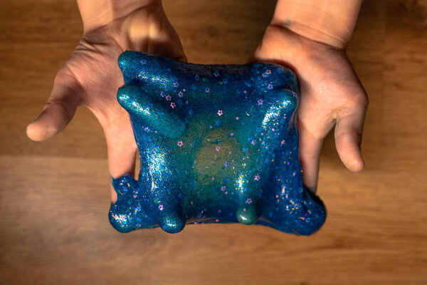 Дети, растягивающие голубую слизь со звёздами, блестят по сторонам. Дети играют в грязные игрушки на деревянном фоне. Делаю слизь. Хобби с модной игрушкой