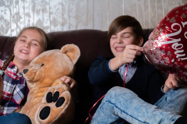 Kırmızı balonla gülümseyen ve mutlu olan erkek ve kız çocuklar kahverengi deri koltukta oturan oyuncak ayı, arkadaşlar, sevgililer günü ya da doğum günü konsepti. Seçici odak