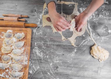 Kadınların elleri ahşap masada un ile hamur tatlısı yapıyor, seçici bir odaklanma ile.