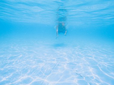 Çocuk havuzda mavi suyun altında yüzüyor, çocuk suyu içiyor. Tatil, yaz tatili, aktif sağlıklı yaşam tarzı, aktivite konsepti.