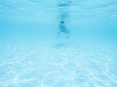 Çocuk havuzda mavi suyun altında yüzüyor, çocuk suyu içiyor. Tatil, yaz tatili, aktif sağlıklı yaşam tarzı, aktivite konsepti.