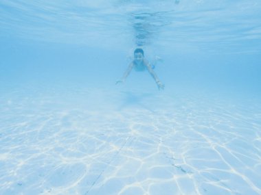 Çocuk havuzda mavi suyun altında yüzüyor, çocuk suyu içiyor. Tatil, yaz tatili, aktif sağlıklı yaşam tarzı, aktivite konsepti.