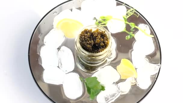 Frasco de vidro com caviar preto no gelo com limão, salsa — Vídeo de Stock