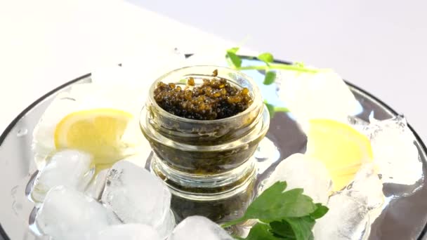 Glass jar with black caviar on ice with lemon, parsley — Stock Video