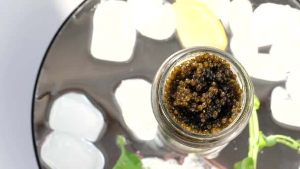 Frasco de vidro com caviar preto no gelo com limão, salsa — Vídeo de Stock