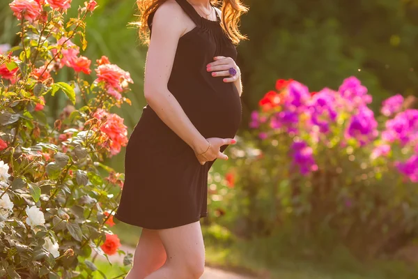 Young beautiful pregnant woman with flowers on the background — Stock Photo, Image