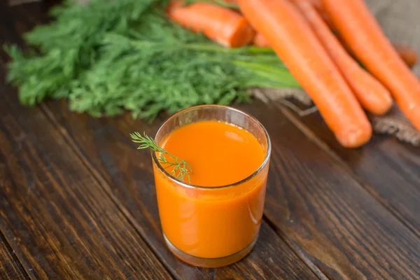 Carrot juice and fresh carrot on a wooden background