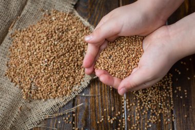 Ahşap arka plan ve elleri üzerinde buğday serpilir