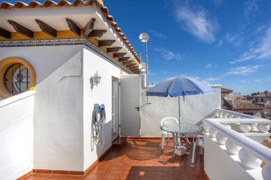 Terasotta fayanslarının yer aldığı parlak çatı terası, şemsiyeli ve sandalyeli cam bir masa, beyaz balyoz ve geleneksel Akdeniz tarzı çatı..