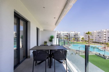 Geniş bir havuz, palmiye ağaçları ve güneşli bir günde şık bir apartman kompleksi olan modern balkon..