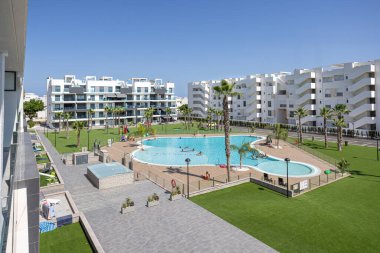 Havuzu, palmiye ağaçları ve çimenliği olan, çağdaş beyaz apartmanlarla çevrili, berrak mavi gökyüzü altında geniş bir yerleşim yeri..