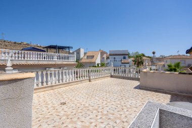 Açık çatı, desenli fayanslar ve beyaz balyoz manzaralı evler ve mavi gökyüzü.