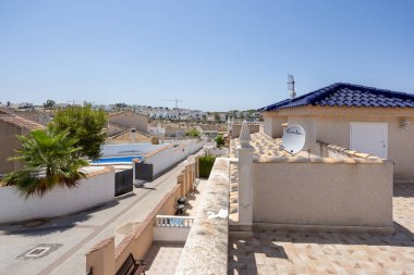 Kiremitli çatıdan manzara sakin bir mahalle, havuz, palmiye ağaçları ve mavi gökyüzünü gösteriyor.