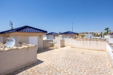 Geniş fayanslı çatı, çoklu depolama üniteleri, yuvarlak masa ve uydu antenleri görünür.