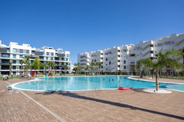 Geniş havuzlu, güneşli, palmiye ağaçlı ve mavi gökyüzü olan modern yerleşim yerleri.