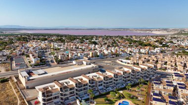 Açık gökyüzü altında pembe tuz gölüne çarpan banliyö konutlarının hava perspektifi