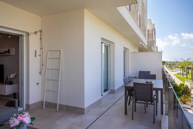 Uzun bir balkon, yemek odası ve manzaralı bir yerleşim yeri manzarası.