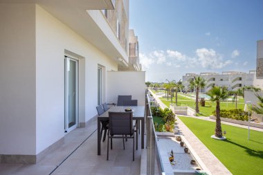 Uzun bir balkon, yemek odası ve manzaralı bir yerleşim yeri manzarası.