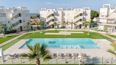 Yüzme havuzu, güneşlik yatakları, peyzaj bahçeleri ve Akdeniz tarzı mimarisi olan bir konut kompleksinin ön görüntüsü..