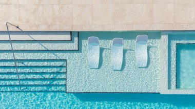 Lüks bir havuzun tepeden tırnağa görüntüsü. Şatafatlı şezlonglar, ışıldayan su ve zarif bir basamak tasarımı..