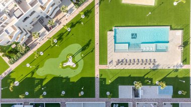 Güneşli bir apartman kompleksinin insansız hava aracı fotoğrafı. Havuz, dinlenme odası ve yürüyüş yolları olan manikürlü bahçeler..