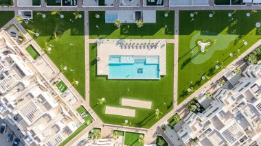 Havuz, spor sahaları, bahçeler ve aile dostu konforların yer aldığı modern bir konut geliştirmenin insansız hava aracı görüntüsü.