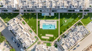 Merkezi havuz, yeşil alanlar, eğlence bölgeleri ve modern mimarinin yer aldığı bir apartman kompleksinin insansız hava aracı görüntüsü..