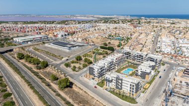 Torrevieja yakınlarındaki modern dairelerin geniş hava görüntüsü, pembe tuz gölü, deniz ve arka planda perakende parkı var..