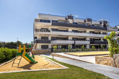 Bahçeler ve çimlerle çevrili küçük bir oyun parkında sarı ve yeşil bir kaydırak içeren çağdaş yerleşim yeri.