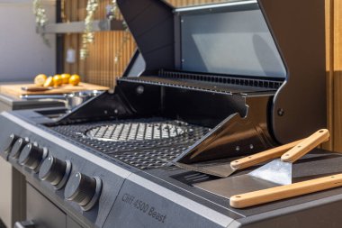 Güneşli bir terasta ahşap saplı aletler ve limonlarla şık bir barbekü ızgarasının ayrıntılı görüntüsü