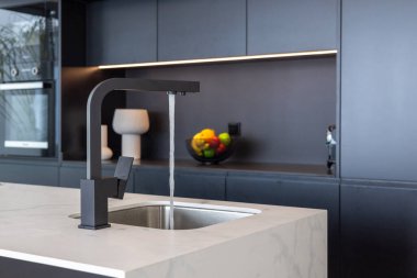 Çağdaş mutfak adası su musluğu, taş yüzeyi ve parlak siyah kabin zeminiyle