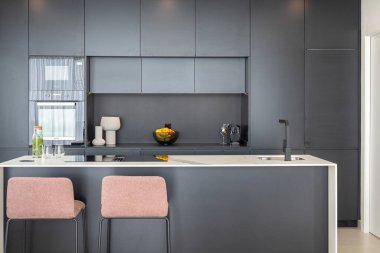 Temiz çizgileri, siyah dolapları, mermer adası ve minimalist dekoru olan çağdaş bir mutfak.