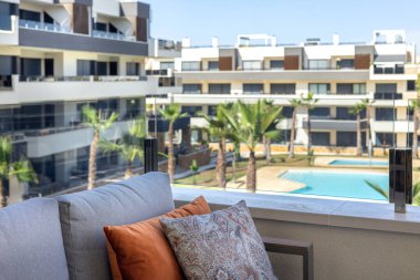 Çağdaş apartman kompleksinde renkli yastıkları ve havuz manzarası olan rahat bir kanepe.