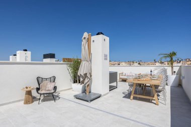 Açık hava mobilyaları, saksı bitkileri ve manzaralı şehir arkaplanı içeren zarif çatı terası.