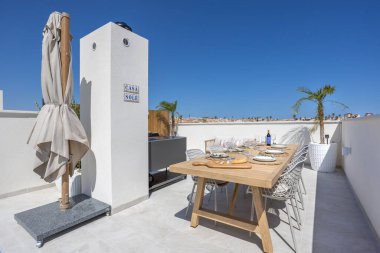 Ahşap masası, sandalyeleri ve mavi gökyüzünün altında palmiye ağaçları olan şık bir çatı yemek alanı.