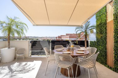 Yemek masası, gölgelik gölgelik, palmiye bitkileri ve şehir manzaralı lüks bir teras.