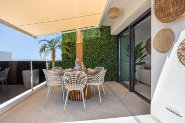 Yuvarlak masalı davetkar teras, gölgelik tente, palmiye bitkileri, ve kapalı alanda rahat erişim