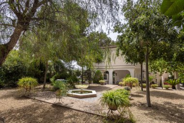 Beyaz Akdeniz tarzı evin önünde çeşme ve yeşillikle gölgeli bahçe avlusu