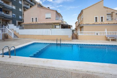 Temiz su, fayans döşeme, basamaklar ve mavi gökyüzünün altındaki evleri çevreleyen yerleşim havuzu