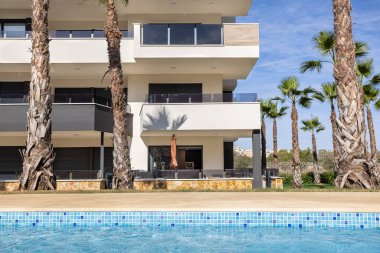 Modern apartment with shaded terrace overlooking swimming pool and palm landscaping