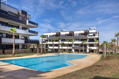 Açık mavi gökyüzünün altında havuzu ve palmiye ağaçları olan modern yerleşim yeri