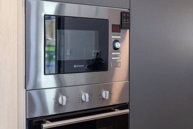 Çağdaş mutfaktaki parlak paslanmaz mikrodalga fırın ünitesine yakın plan.