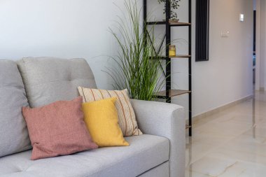 Parlak oturma odasının içinde gri bir kanepe, renkli yastıklar ve minimalist raf dekoru var.