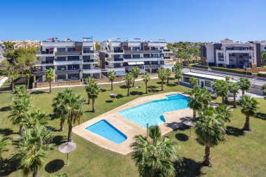 Güneşli Torrevieja 'daki Amanecer apartmanlarında palmiye ağaçlarıyla çevrili geniş ortak havuz alanı.