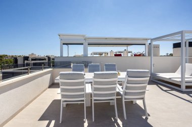 Amanecer tatil dairelerinde yemek sandalyeleri ve şezlongları olan güneşli çatı terası..